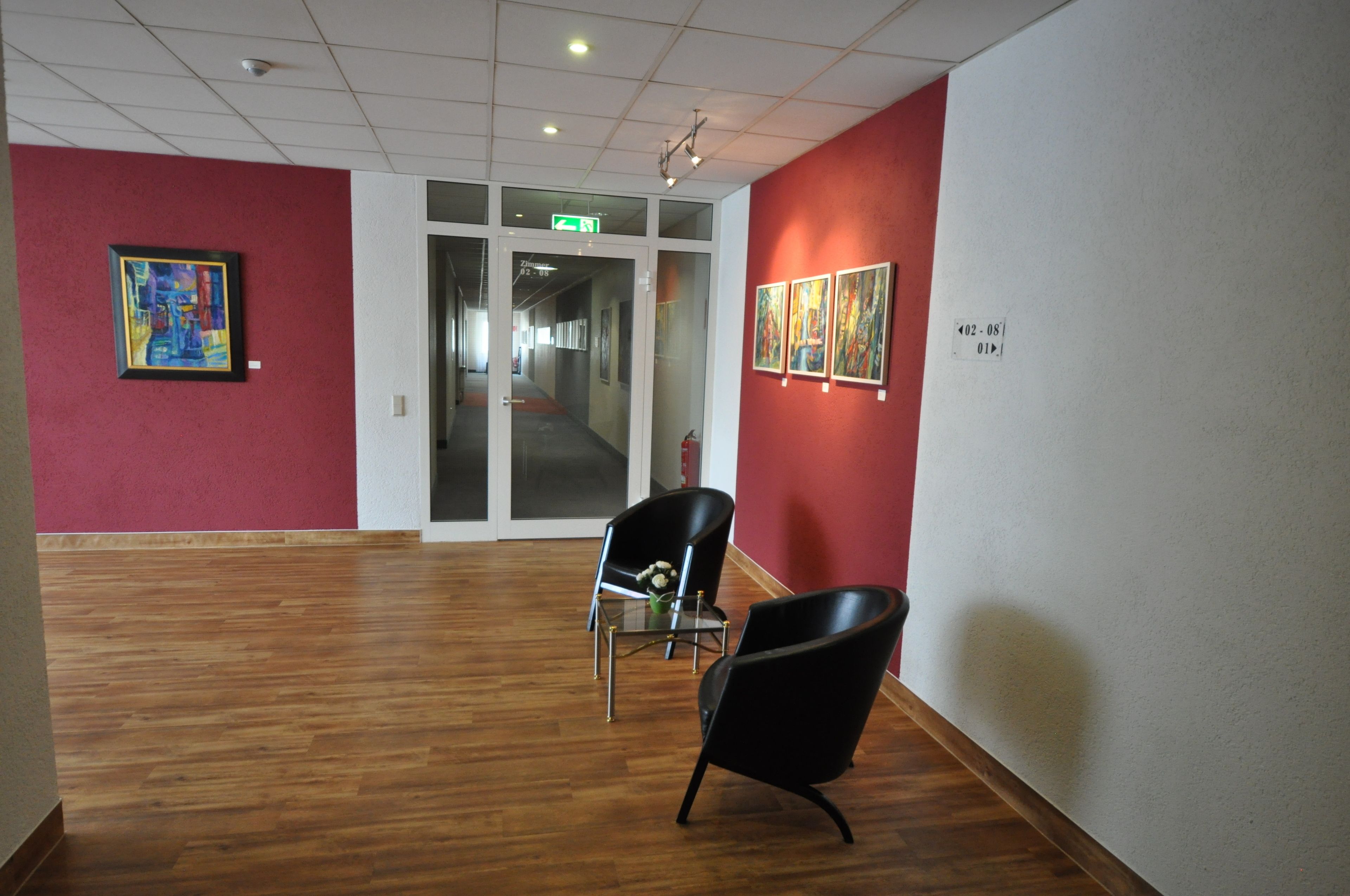 An art gallery with wooden floors, red walls, and black chairs.