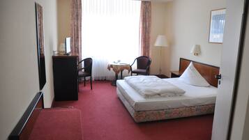 Una habitación de hotel con cama, escritorio, silla, mesita y lámpara.