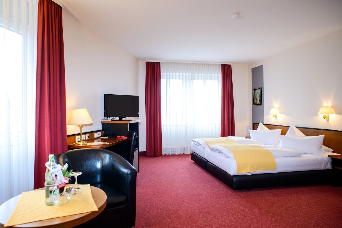 A hotel room with a bed, a desk with a chair, a television, and a window with curtains.