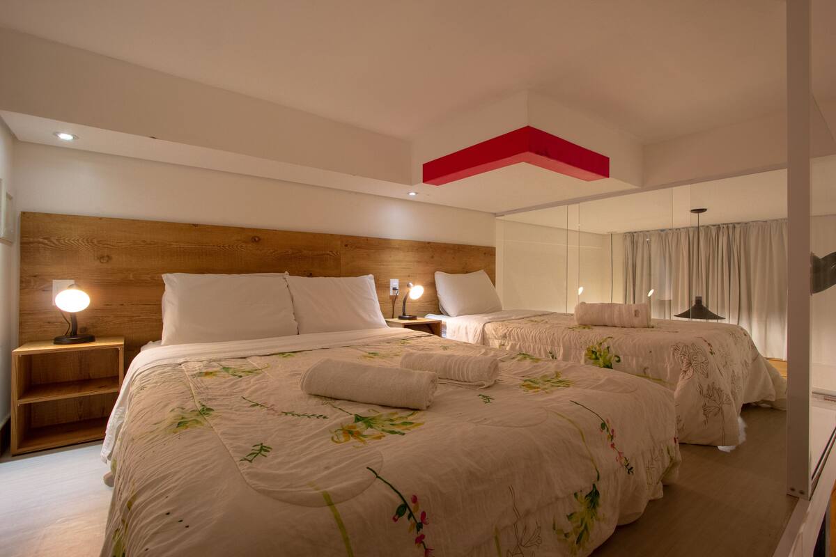 A hotel room with two beds, a wooden headboard, bedside lamps, and a large window with curtains.