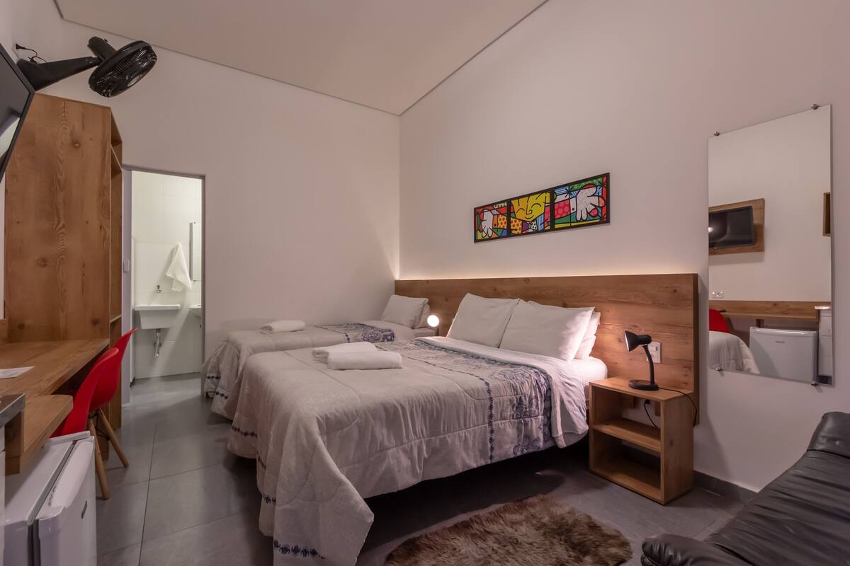 A modern bedroom with two beds, a desk, a chair, a small table, a mirror, and a wall art piece.