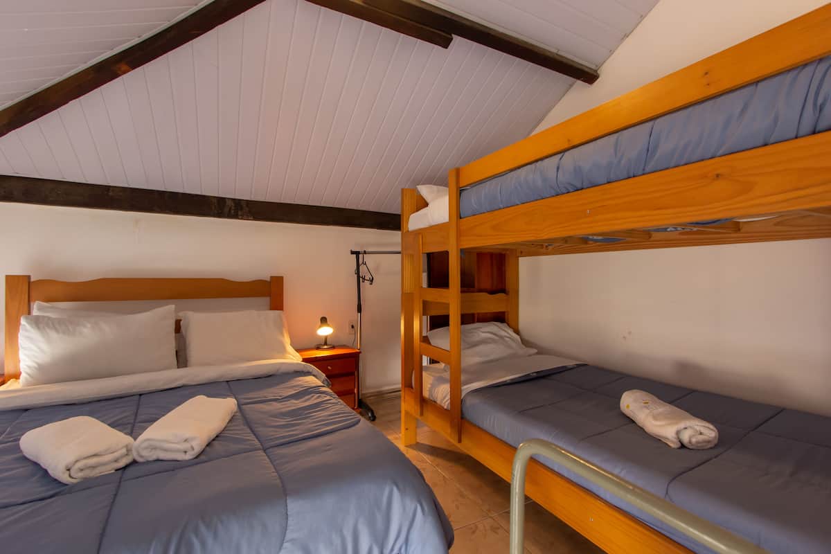 A room with two bunk beds, a bedside table with a lamp, and neatly folded towels on the beds.