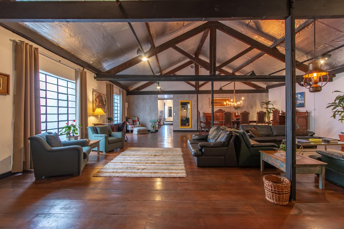 A spacious living room with wooden flooring, multiple sofas, a coffee table, and a large window with curtains.