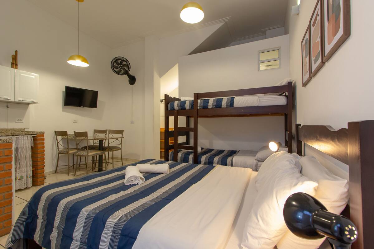A hotel room with bunk beds, a TV, a desk with chairs, and a small kitchen area.