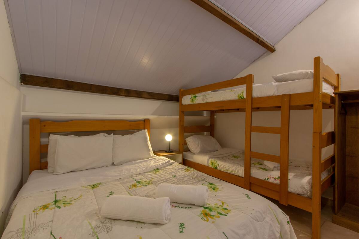 A dormitory room with bunk beds, a bedside table with a lamp, and a floral-patterned bedspread.