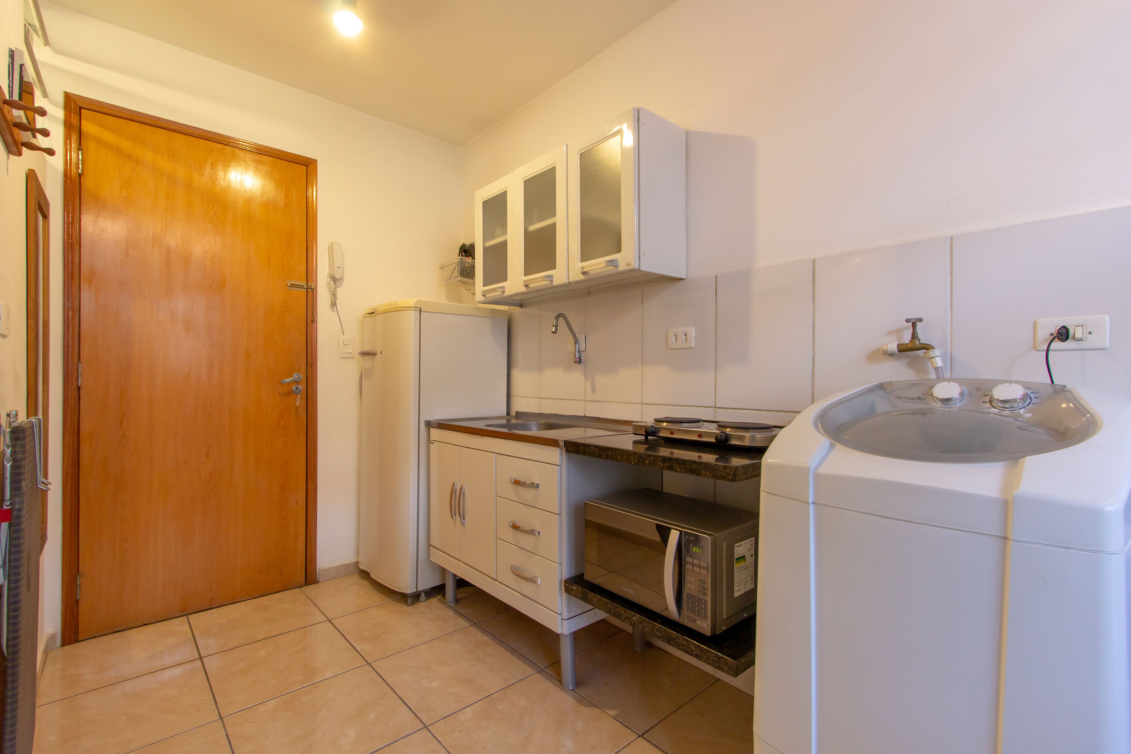 A compact kitchen with a wooden door, white cabinets, a microwave, and a sink.