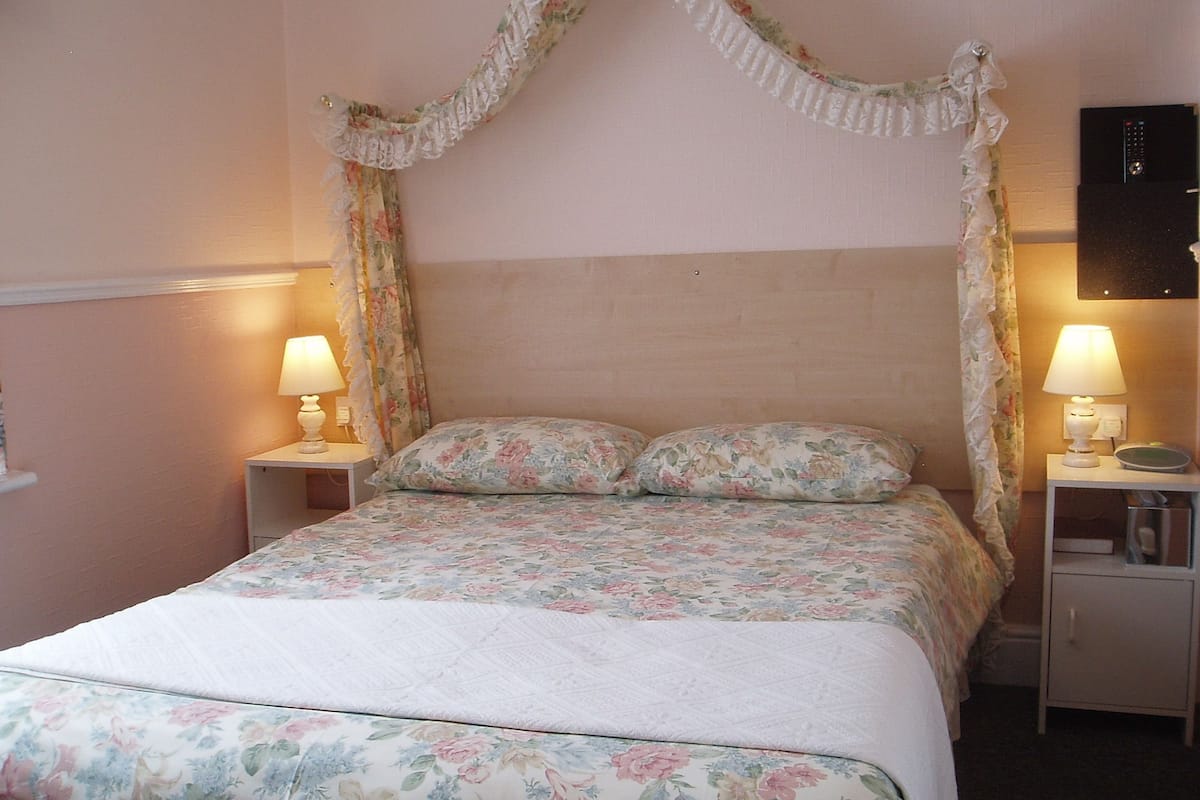 A bedroom with a canopy bed, floral bedding, two bedside lamps, and a nightstand with a lamp.