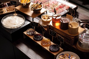 A buffet with various food items and condiments, including Greek yogurt, honey yogurt, and different jams.