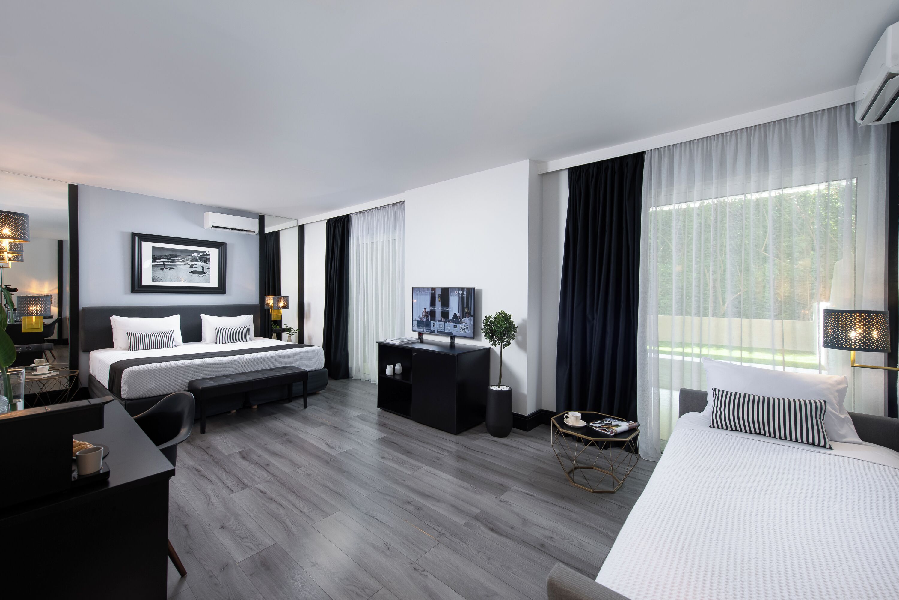 A modern hotel room with a large bed, a desk, a TV, and a sofa.
