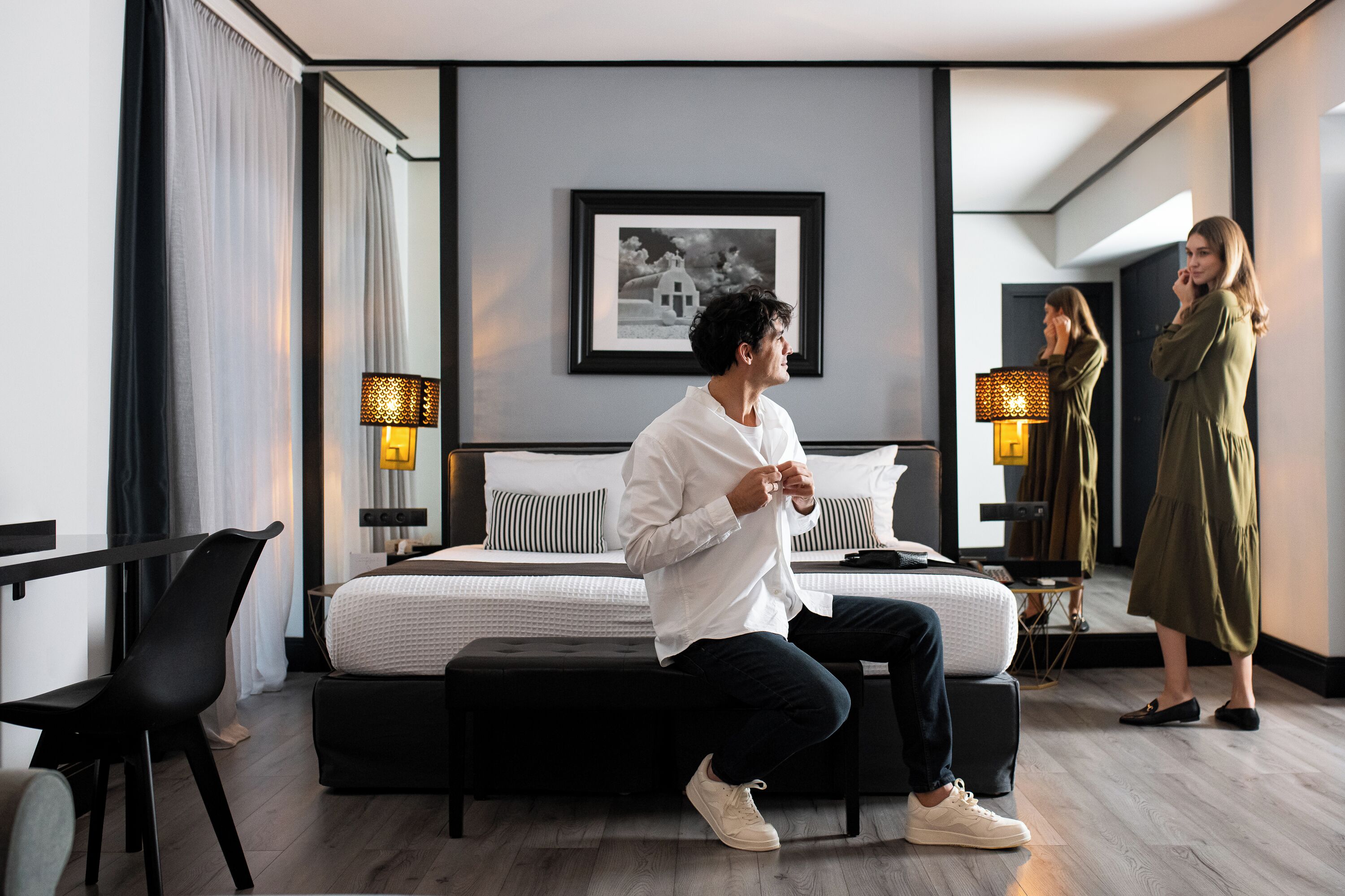 A modern hotel room with a large bed, a bedside table, a chair, and a mirror.