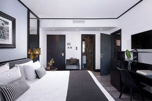 Habitación de hotel moderna con una cama grande, un escritorio, un televisor y un baño visible a través de una puerta abierta.