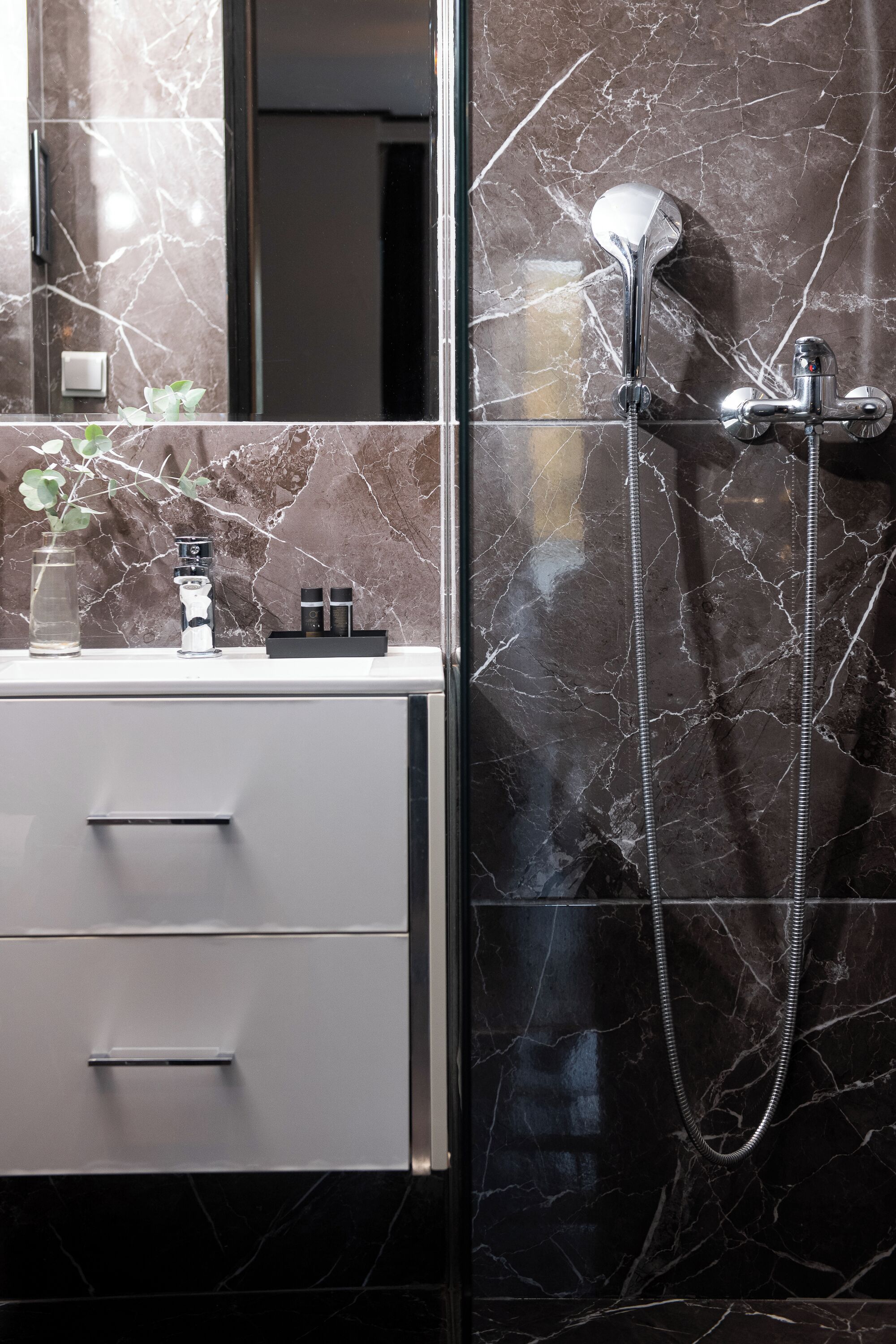 A bathroom with a marble backsplash, a modern sink, and a shower with a handheld showerhead.
