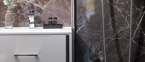 A bathroom with a marble backsplash, a modern sink, and a shower with a handheld showerhead.
