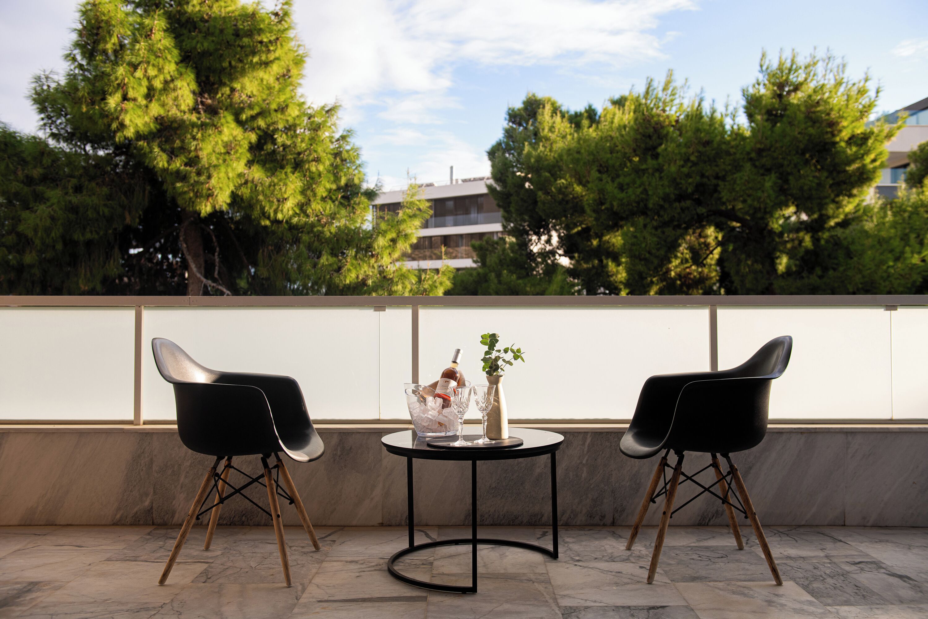 Um terraço com duas cadeiras pretas, uma mesa redonda pequena e um vaso com uma planta.
