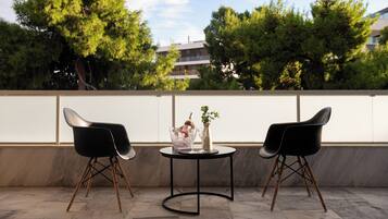 A terrace with two black chairs, a small round table, and a vase with a plant.