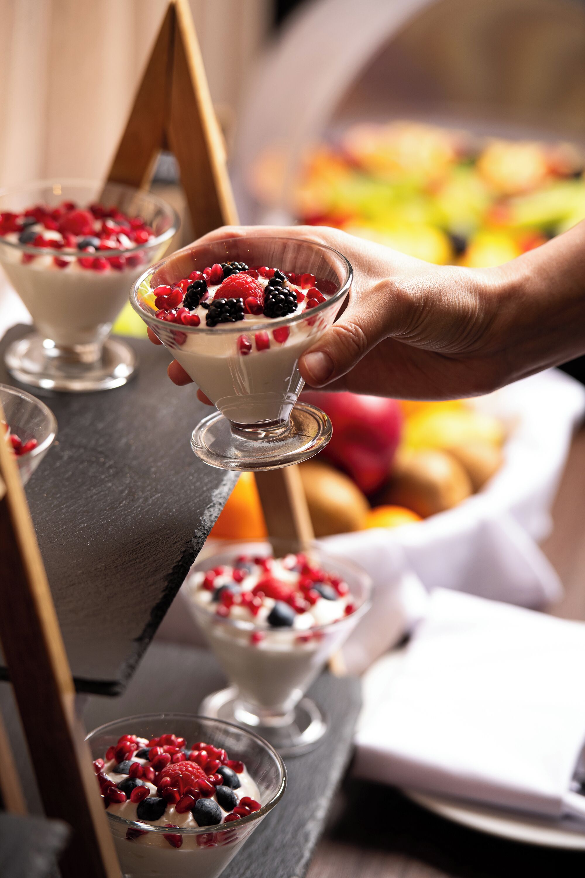 A dessert tray with three bowls of yogurt topped with berries, held by a hand.