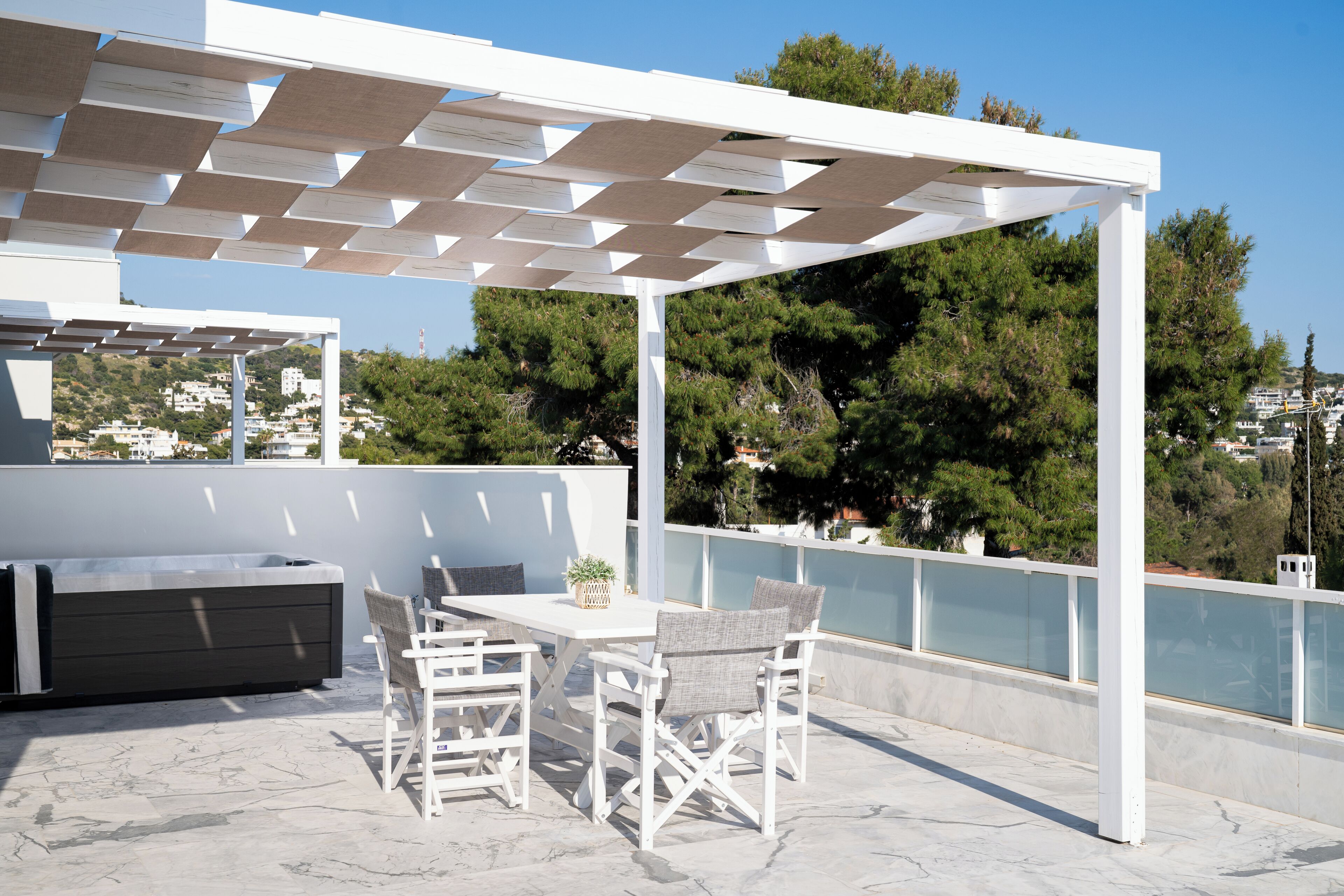Un patio al aire libre con una pérgola blanca, una mesa con sillas y un banco incorporado.