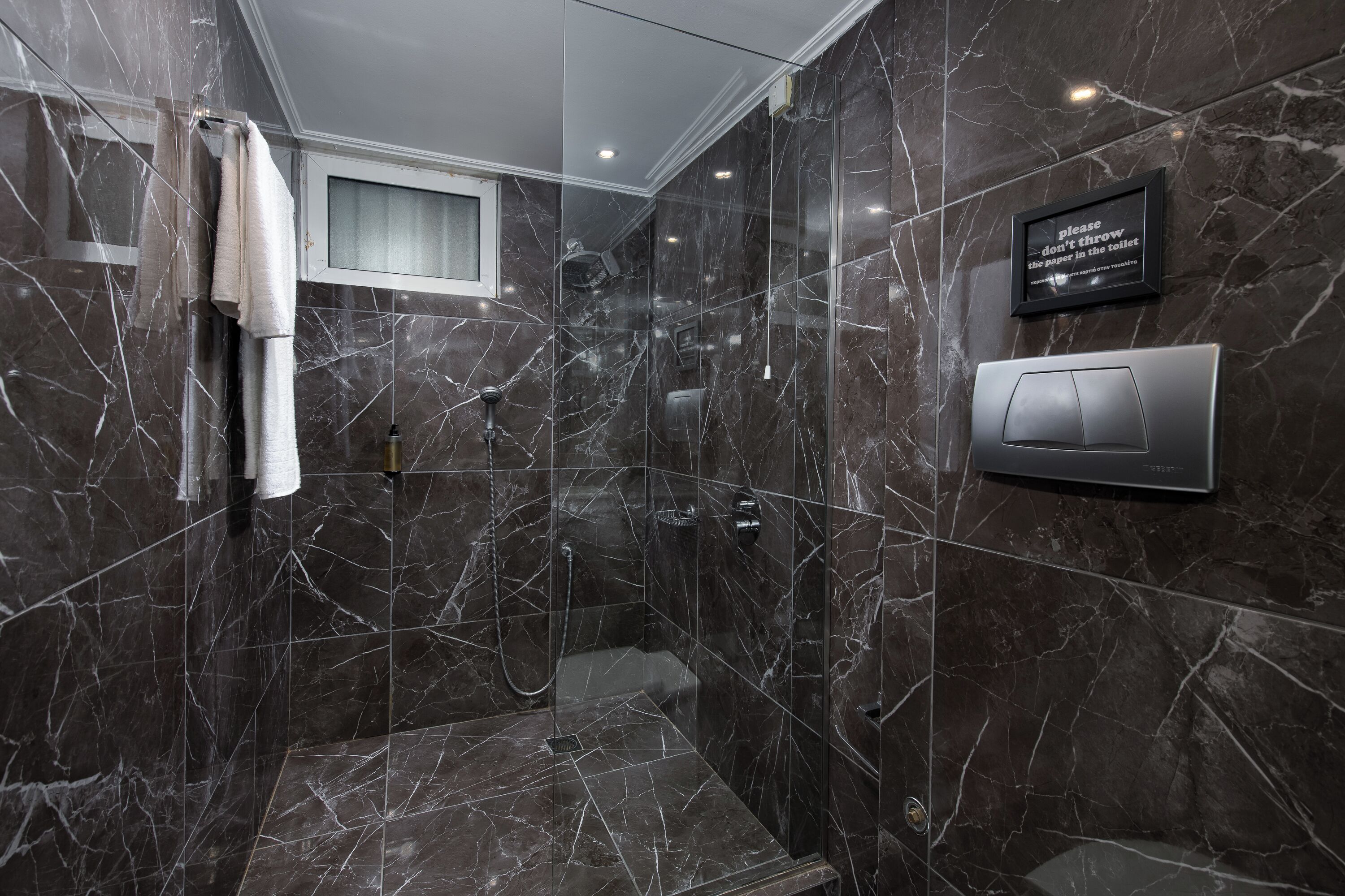 A modern bathroom with a glass-enclosed shower, marble walls, and a towel rack.