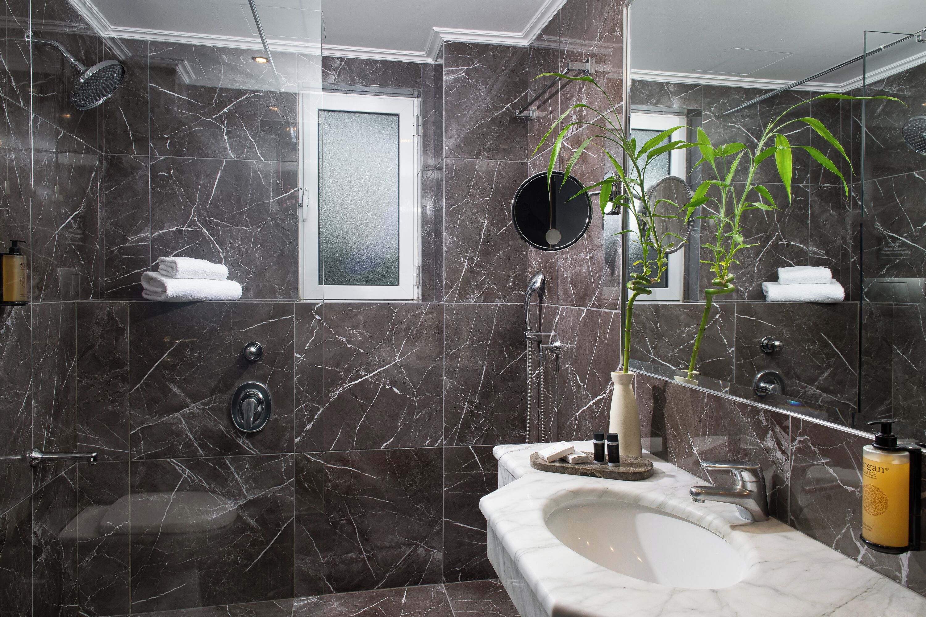 Un baño moderno con pared de mármol, una bañera, un lavamanos con espejo y una zona de ducha.