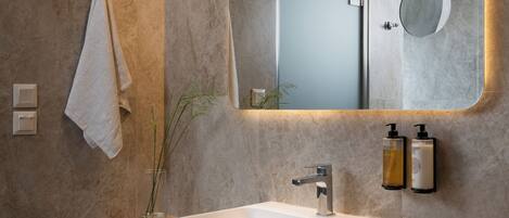 A modern bathroom with a large mirror, a white sink, and a bench.