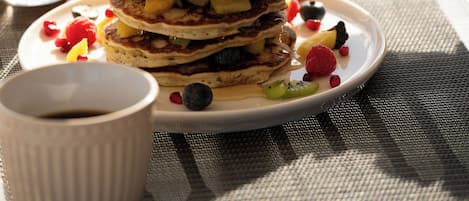 A stack of pancakes with syrup being poured on top, accompanied by a glass of orange juice and a cup of coffee.
