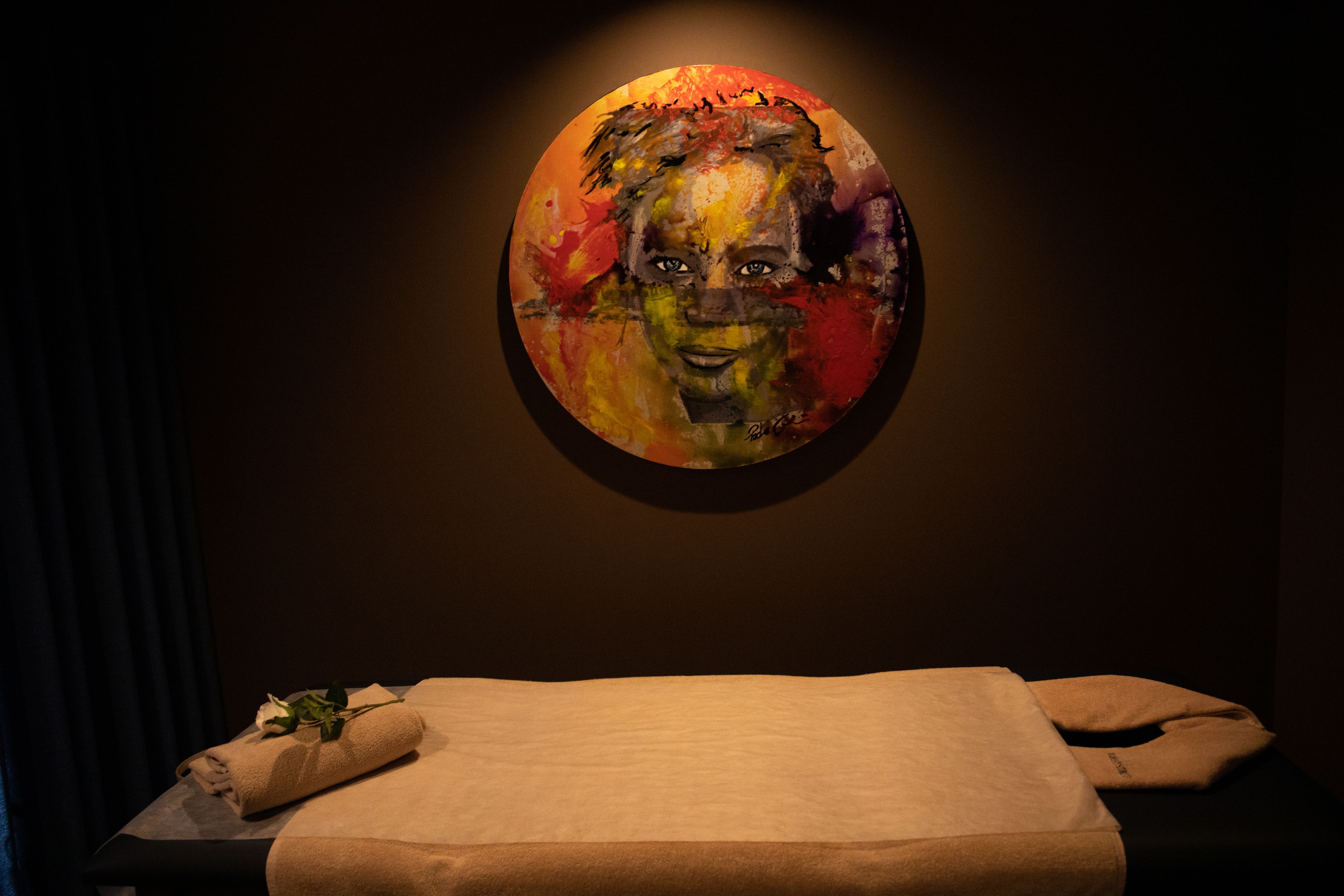 A massage therapy room with a massage table, a towel, and a wall-mounted painting.