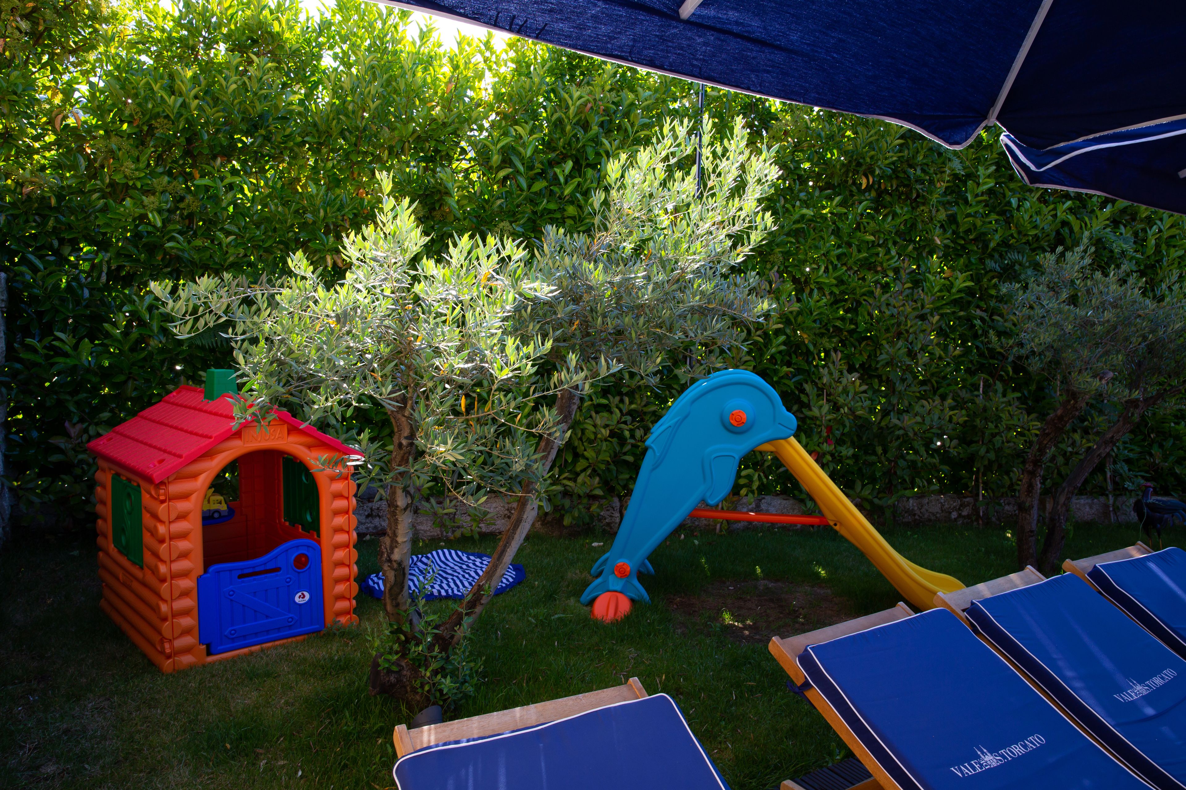 A children's play area with a small playhouse, a slide, and a swing set.