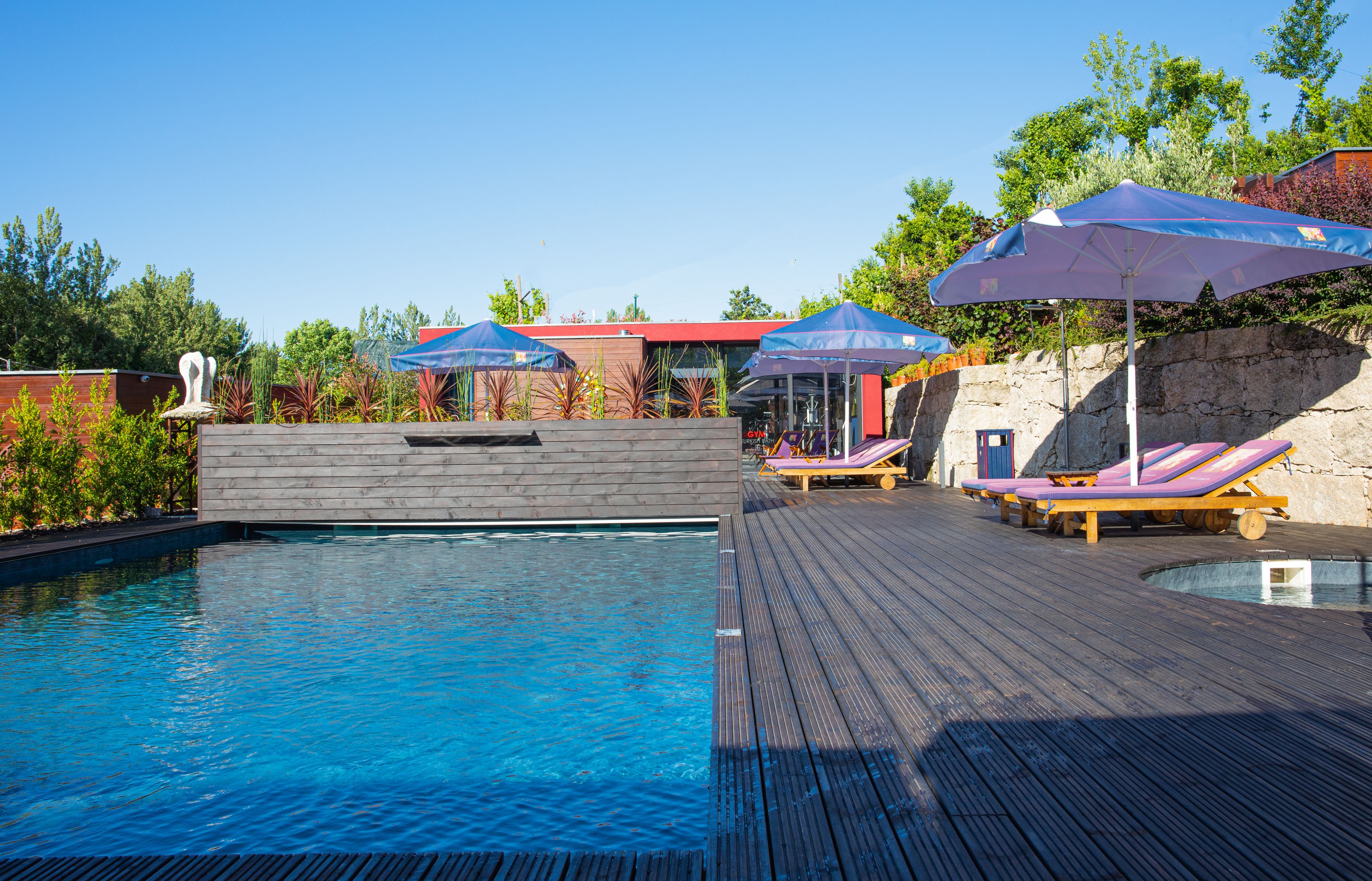 A pool area with wooden deck, lounge chairs, and umbrellas.