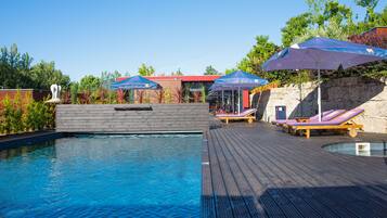 A pool area with wooden deck, lounge chairs, and umbrellas.