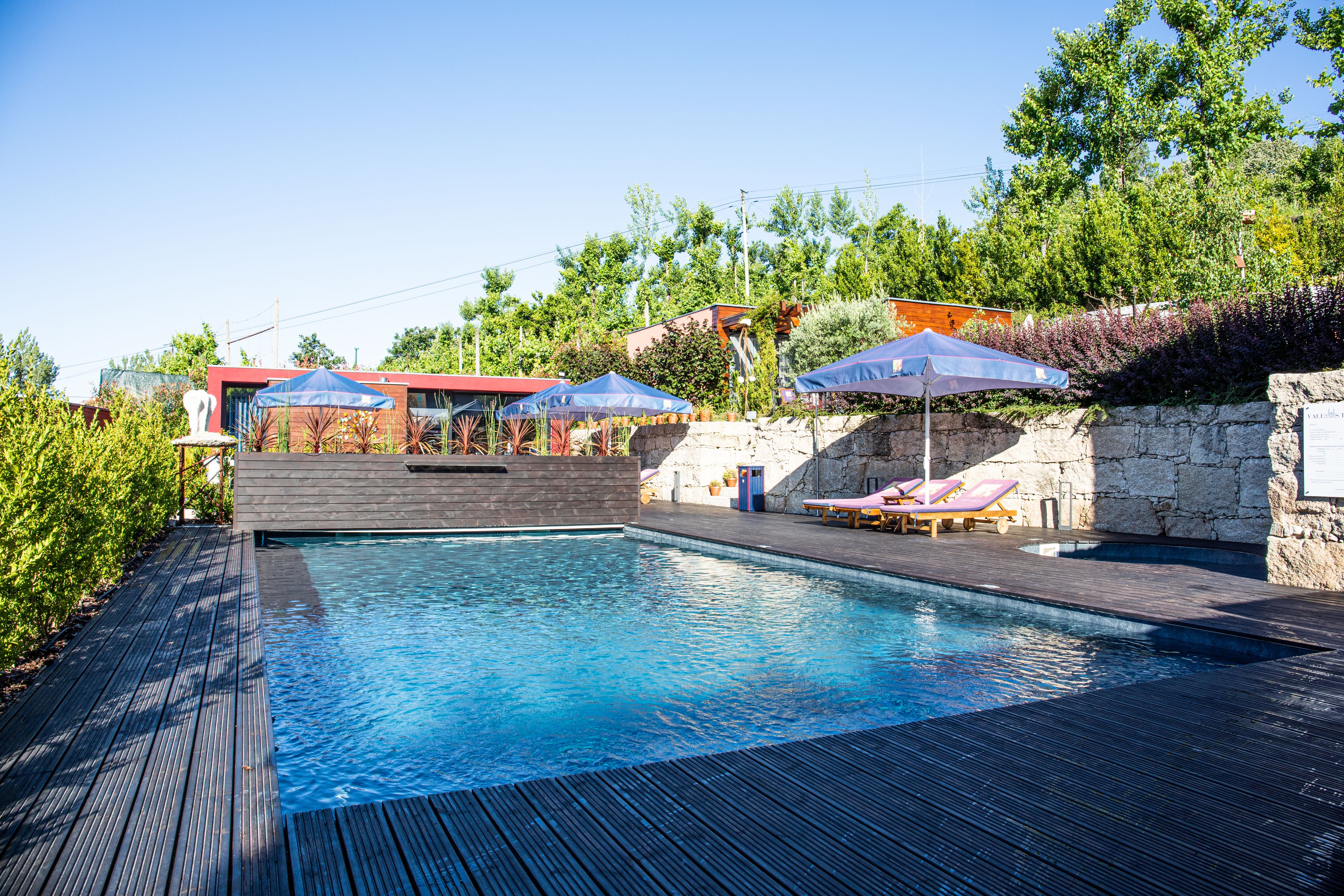 Une piscine entourée d’une terrasse en bois, de chaises longues et de parasols.