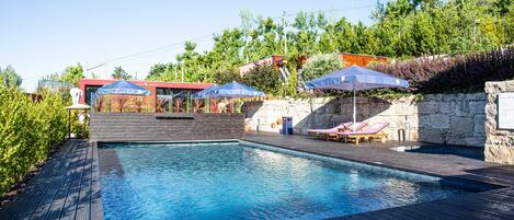 A swimming pool with wooden decking, lounge chairs, and umbrellas.