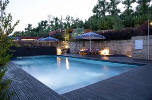 Piscina con sillas de descanso y sombrillas, rodeada de muros de piedra y vegetación.