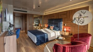 Una habitación de hotel moderna con una cama grande, un escritorio con lámpara, una silla roja y una mesa redonda.