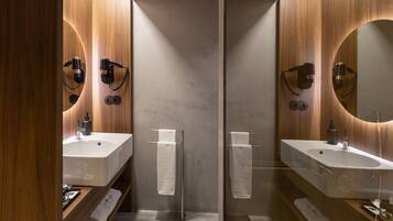 Une salle de bain moderne avec deux lavabos, une cloison en verre, un lambris en bois et un grand miroir.