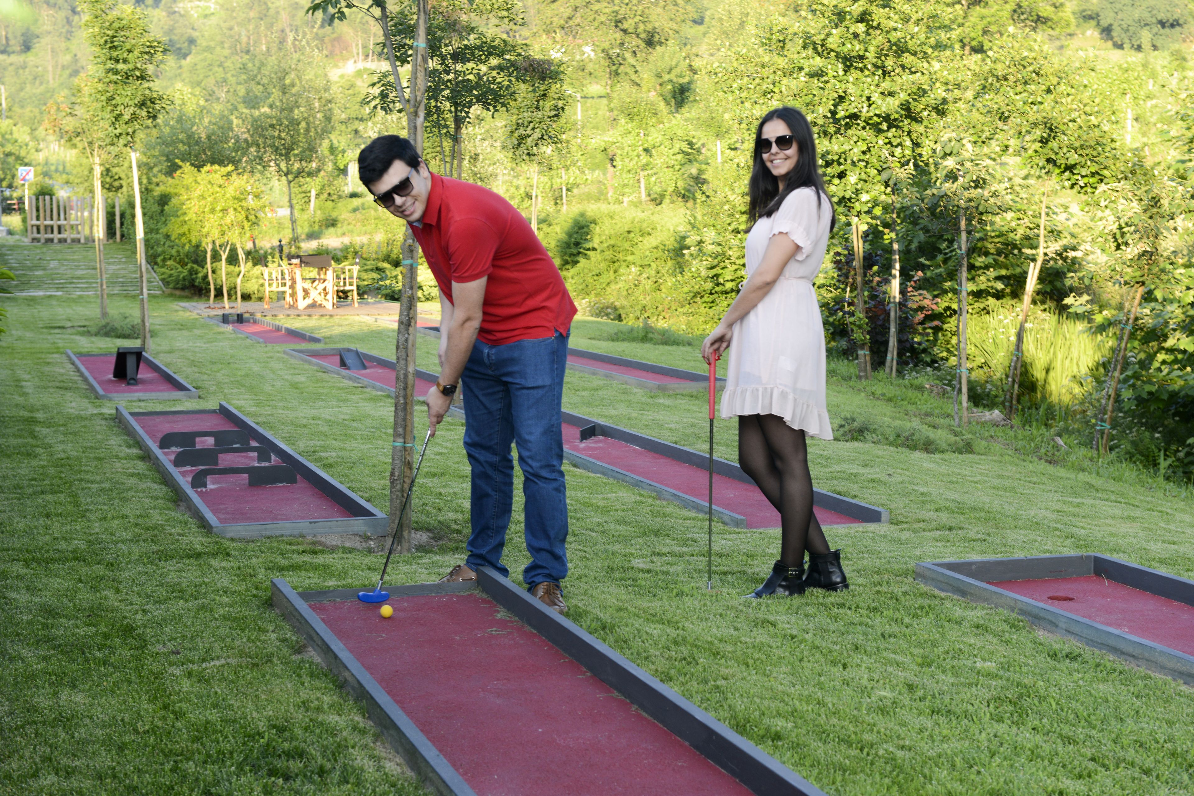 Um campo de croquet com grama vermelha e verde, estacas de madeira e uma construção de madeira ao fundo.