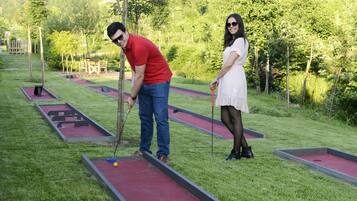 Um campo de croquet com grama vermelha e verde, estacas de madeira e uma construção de madeira ao fundo.