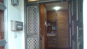 Een kamer met een houten deur, een metalen boekenkast en een klein bureau met een lamp.