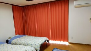 Een kamer met twee bedden, een blauw kamerkleed met patroon, houten vloer, rode gordijnen en een airconditioning.