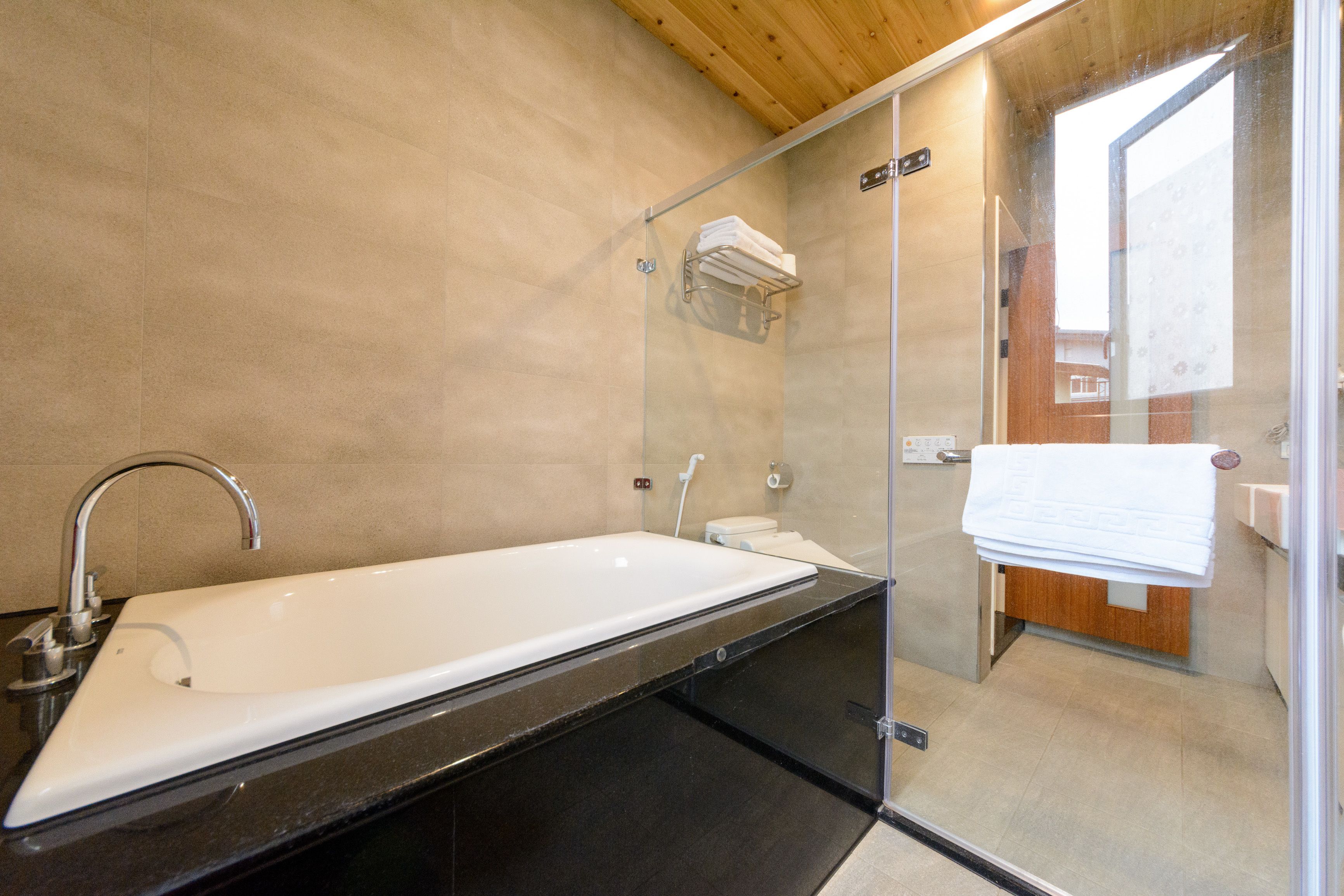 A modern bathroom with a large white bathtub, a glass-enclosed shower, and a wooden ceiling.
