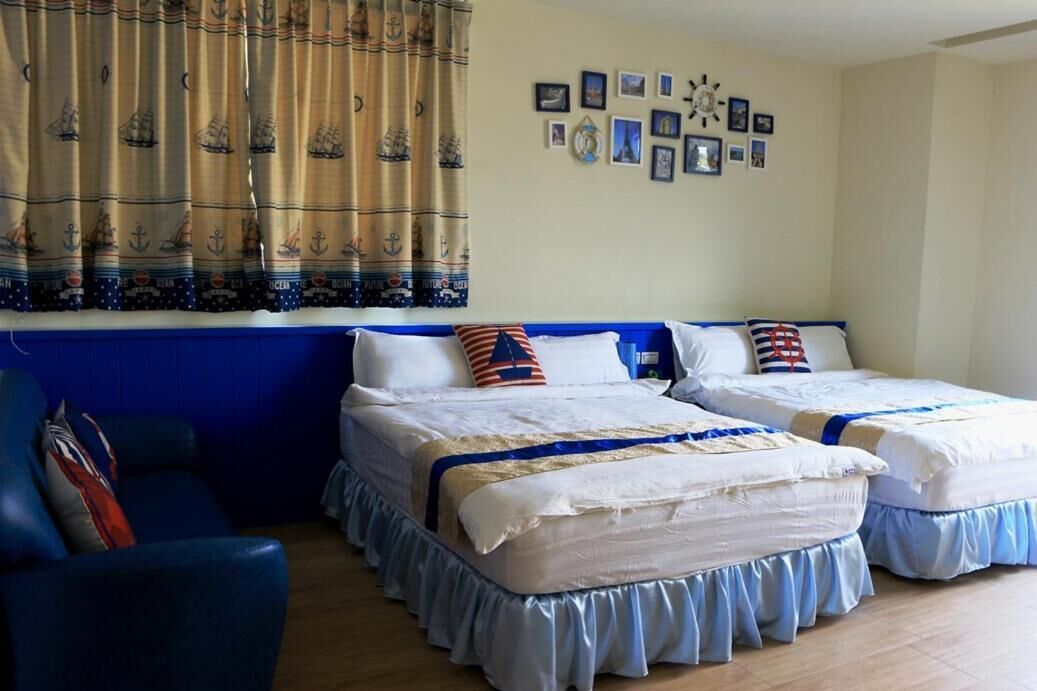 Ein Zimmer mit zwei Betten, einem blauen Sessel und einem Vorhang mit Meeresmotiven.