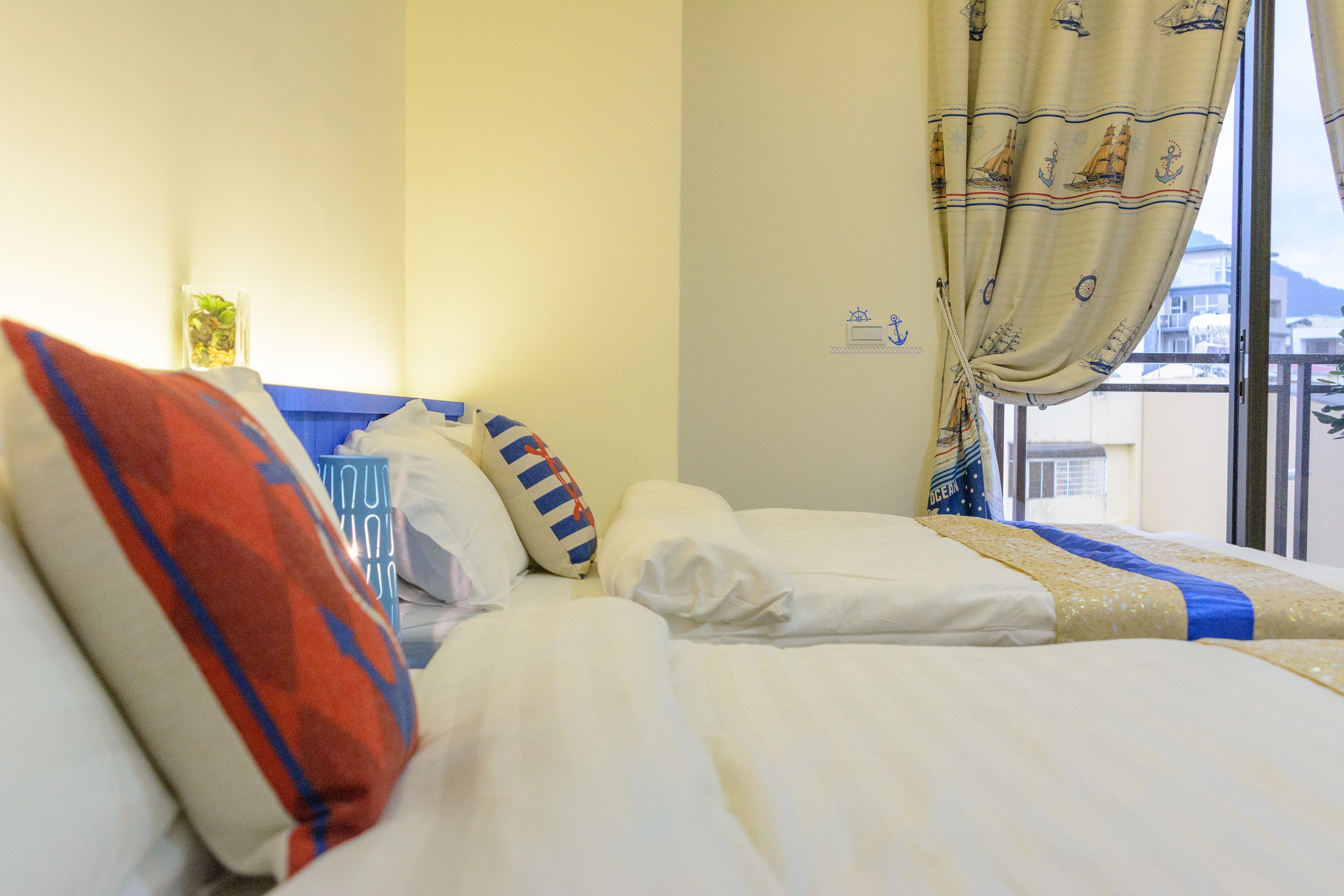 A hotel room with a bed, pillows, a window with curtains, and a view of buildings outside.