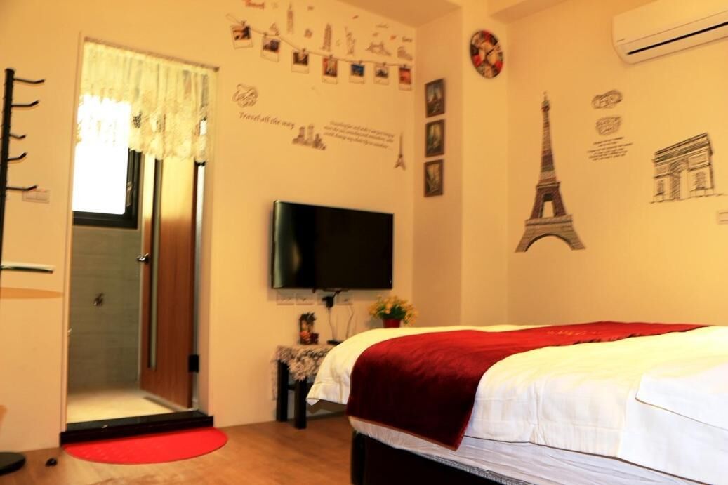Una habitación de hotel con una cama, un televisor, una puerta con espejo y adornos de pared que incluyen la Torre Eiffel.