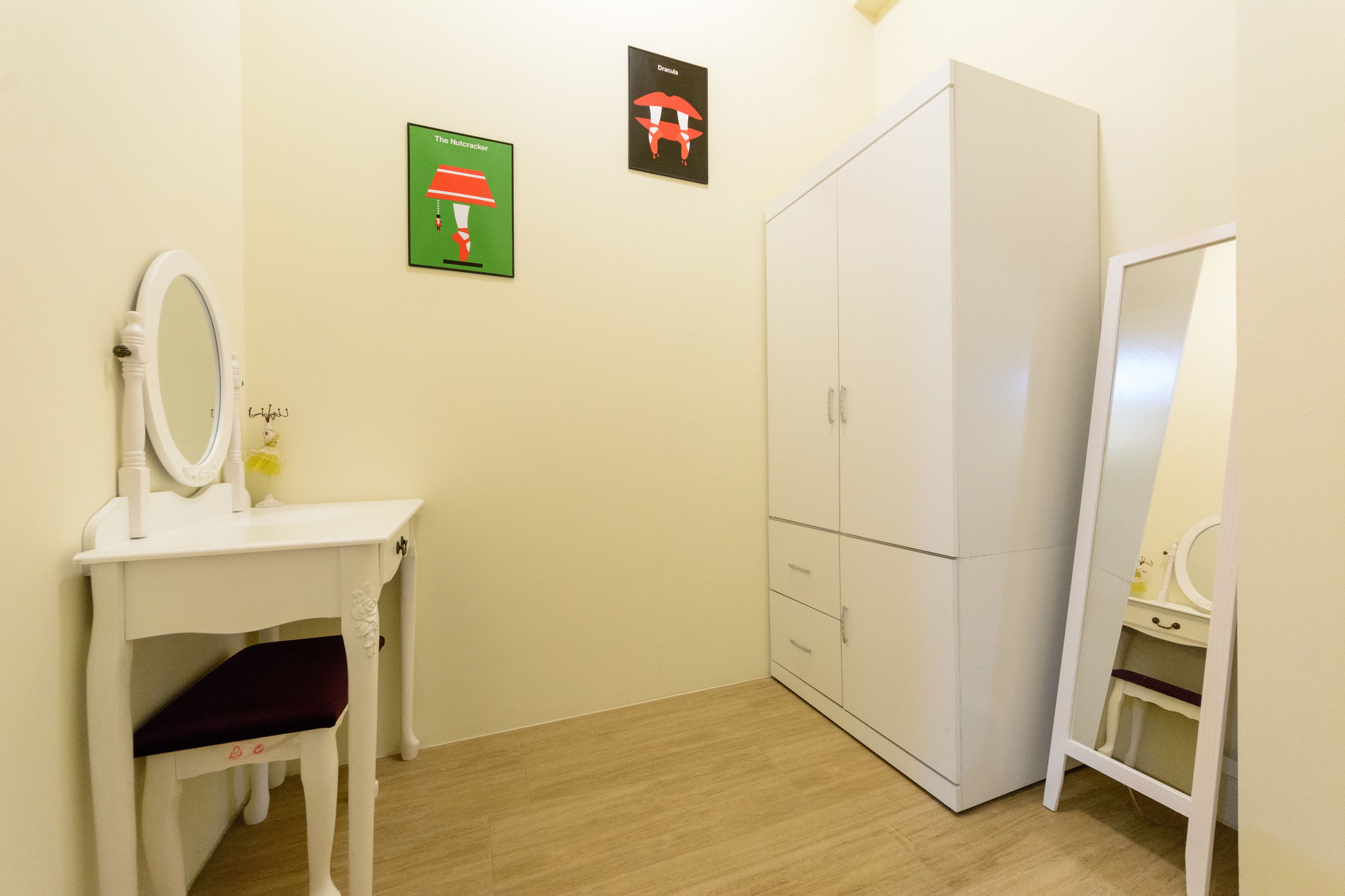 A small, clean room with a white vanity, a mirror, a wardrobe, and two wall-mounted pictures.