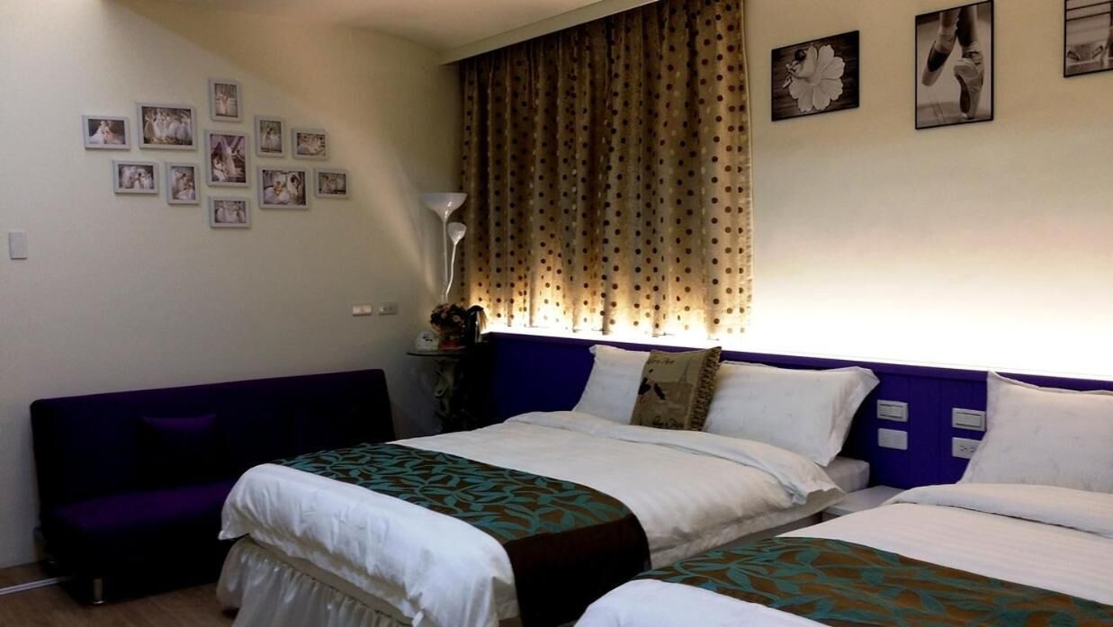 A bedroom with two beds, a purple sofa, and a wall adorned with framed photos.