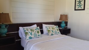 A neatly made bed with white bedding and two decorative pillows with a marine theme. There are two nightstands with lamps and decorative vases. - Sosua villa tropical retreat with ocean views (Sosúa)