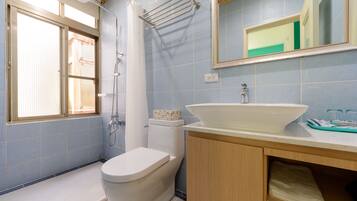 A bathroom with a toilet, sink, shower, and a window.