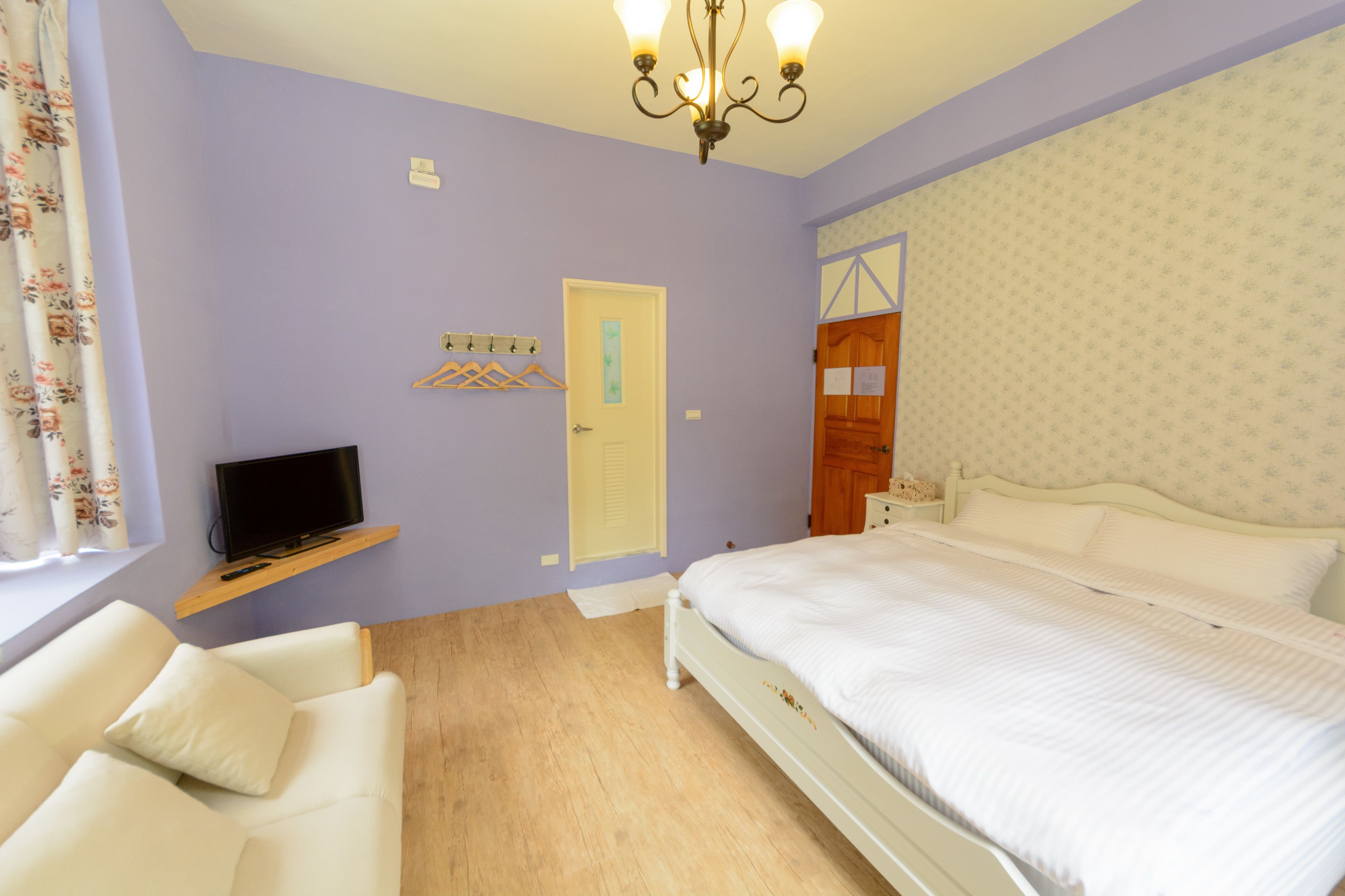 Un dormitorio con una cama, un televisor en un estante, una silla y una puerta.