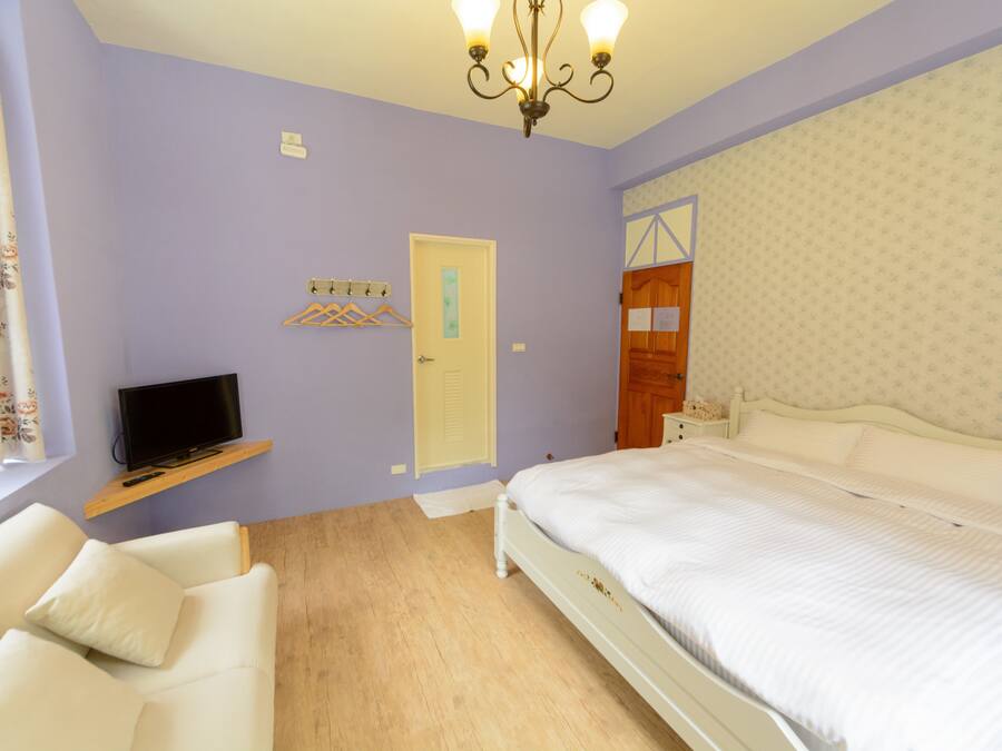 Un dormitorio con una cama, un televisor en un estante, una silla y una puerta.
