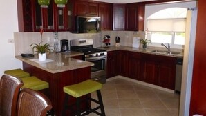 A kitchen with dark wooden cabinets, a central island with stools, a stove, and a microwave. - Touch of elegance! 6 Bedroom near the beach (Sosúa)