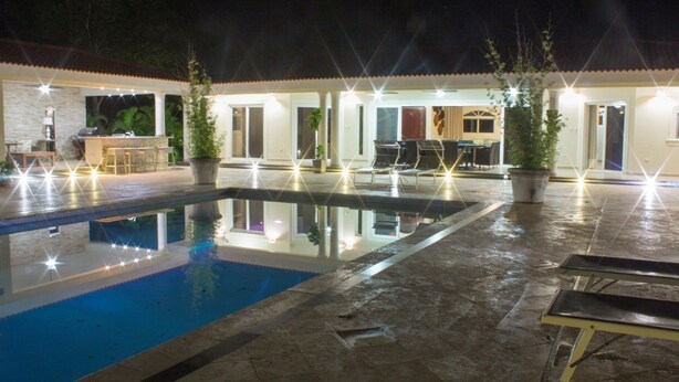 A nighttime pool area with a clear pool, outdoor seating, and well-lit pathways. - Touch of elegance! 6 Bedroom near the beach (Sosúa)